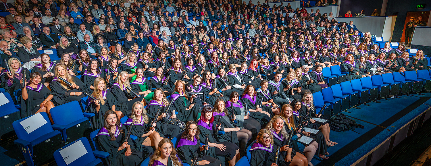 Graduates in robes holding scrolls sitting in an audience Graduates in robes holding scrolls sitting in an audience